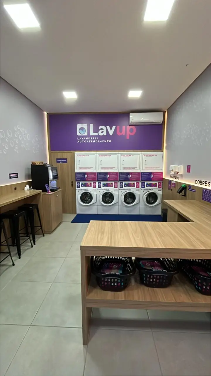 Interior da LAVUP Gramado com mesa para dobrar roupa, cestos, banquetas e máquinas ao fundo